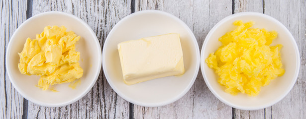A block of butter, margarine and ghee in white bowls over rustic wooden background