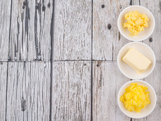A block of butter, margarine and ghee in white bowls over rustic wooden background