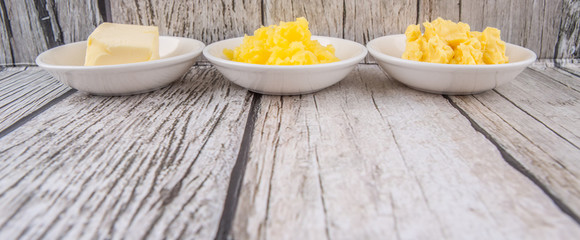 A block of butter, margarine and ghee in white bowls over rustic wooden background