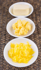 A block of butter, margarine and ghee in white bowls over wicker background