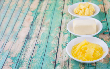 A block of butter, margarine and ghee in white bowls over rustic wooden background