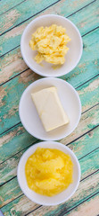 A block of butter, margarine and ghee in white bowls over rustic wooden background