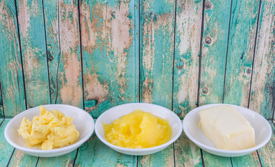 A block of butter, margarine and ghee in white bowls over rustic wooden background