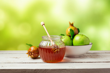 Honey jar and fresh apples with pomegranate over green bokeh background