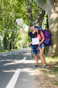 cheerful young couple backpacker hitchhiking on a roadside in summer vacation