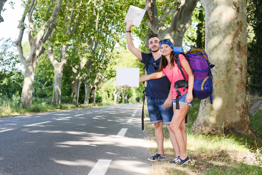 cheerful young couple backpacker hitchhiking on a roadside in summer vacation