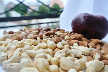 Closeup of a pile of various nuts with a red apple in the background. Healthy/clean eating concept; fresh, organic, unprocessed food; paleo diet.