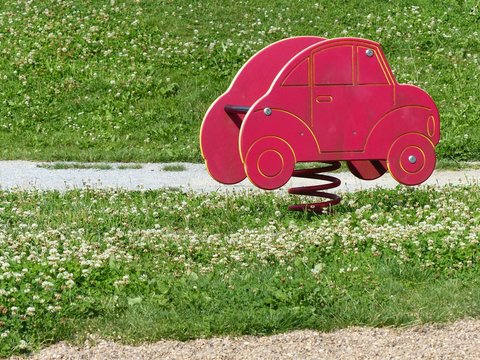 Rotes Auto als Federwippe auf gr&uuml;ner Wiese im Sommer bei Sonnenschein auf dem Mehrgenerationen Spielplatz  in Greste und Asemissen bei Leopoldsh&ouml;he und Bielefeld in Ostwestfalen-Lippe