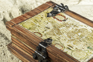Detail of wooden chest with a portolan on its cover, on the beach sand
