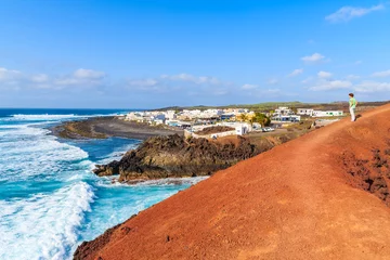 Foto op Canvas Young woman tourist standing on red lava rocks and looking at ocean waves, El Golfo, Lanzarote, Canary Islands, Spain © pkazmierczak