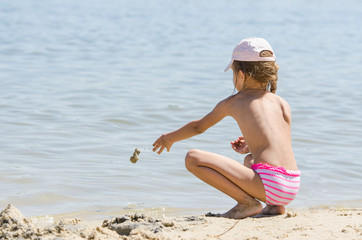 Girl on the river throws sand in water