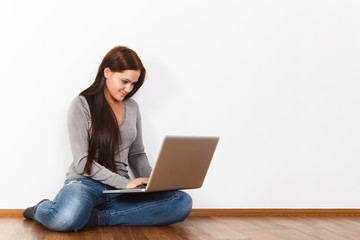 Fototapeta premium Beautiful young woman sitting on floor with laptop