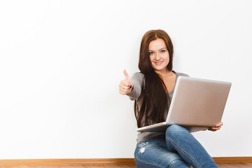 Beautiful young woman sitting on floor with laptop. Thumbs up