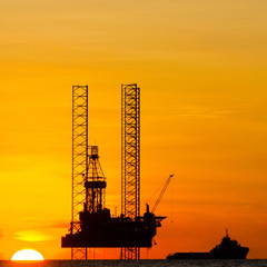 Silhouette of an offshore drilling rig and supply vessel at sunset