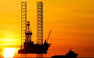 Obraz premium Silhouette of an offshore drilling rig and supply vessel at sunset