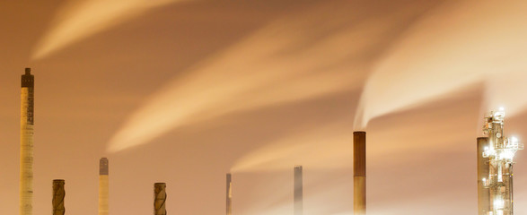 Panoramic image of smoke and chimneys of a large oil-refinery plant at night