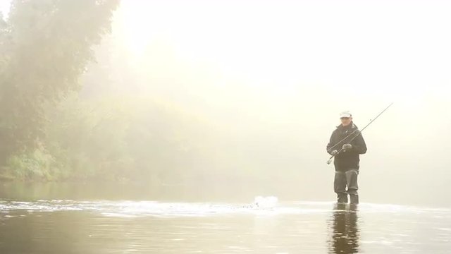 Man Reeling In A Fish From A River Enveloped By Fog