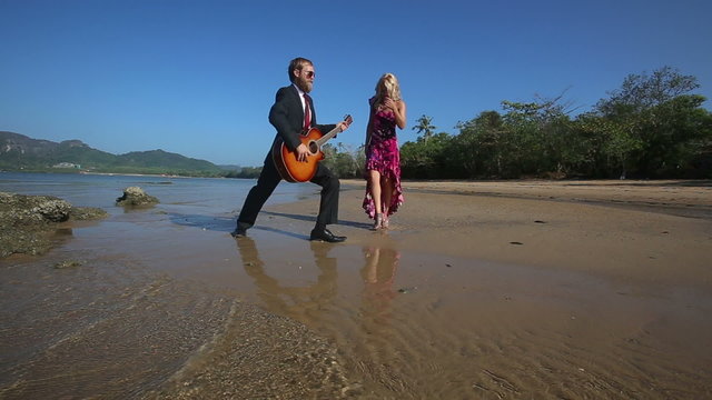 bearded guitarist plays inspiredly and girl in high heel shoes disturbs under low tide