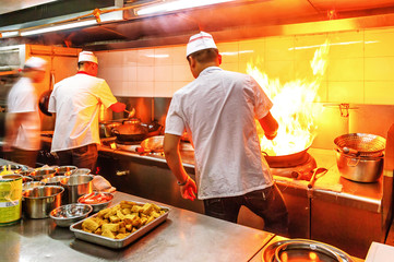 Chef in restaurant kitchen at stove with pan, doing flambe on food