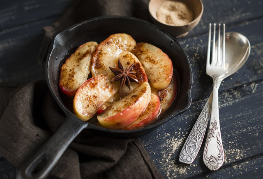 caramelized apples with cinnamon in a vintage pan on a dark wooden background