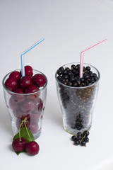 Two Glasses of Fruit.  Cherries and blackcurrants in separate glasses, each with a straw, on a white background.