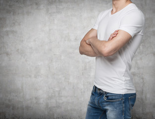 Fototapeta na wymiar Side view of a person in a white V shape t-shirt with crossed hands. Concrete wall on background.