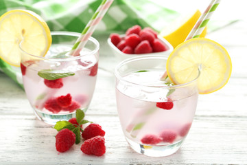 Raspberries and juice in glass on white wooden background