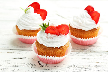 Tasty cupcake with strawberry on white wooden background