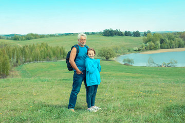 Naklejka na ściany i meble Portrait of grandfather and granddaughter in a landscape of open space Old man photographer on a camping trip with his granddaughter.