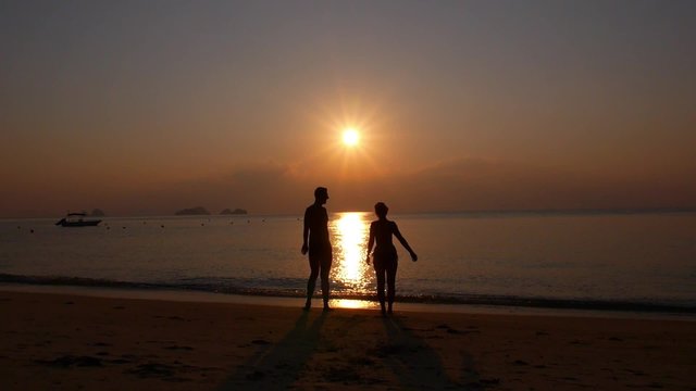 Happy Cheerful Couple Enjoying Sunset at Beach with Arms Raised