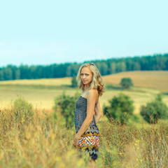 Naklejka na ściany i meble beautiful blonde walks into the field. portrait of a beautiful blonde in a field in spring