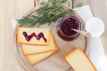 Sliced cheese and cherry sauce on a wooden board with dill and rosemary