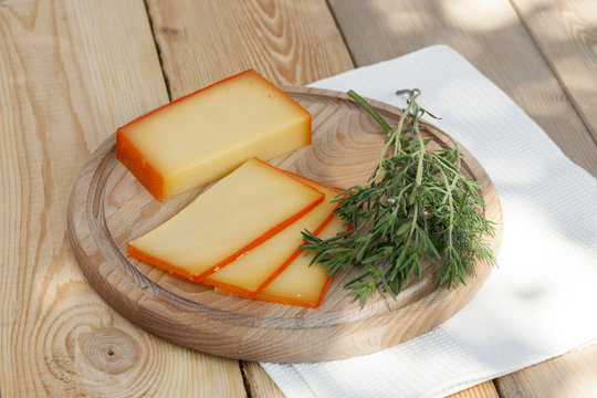 Sliced cheese on wooden board with dill and rosemary, selective focus