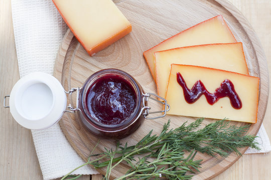 Sliced cheese and cherry sauce on a wooden board with dill and rosemary