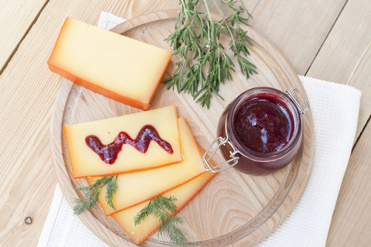 Sliced cheese and cherry sauce on a wooden board with dill and rosemary