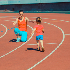 Obraz premium Mother & little daughter running around the stadium. Child runs away from mom at the stadium.