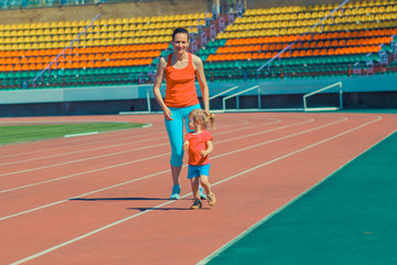 Fototapeta premium Mother & little daughter running around the stadium. Child runs away from mom at the stadium.