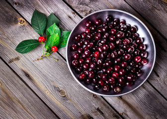 Cherry in metal bowl on old wooden background.
