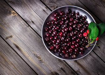 Cherry in metal bowl on old wooden background.
