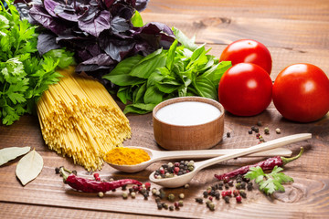 Raw pasta, vegetables, basil and spices on the wood table