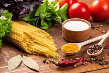 Raw pasta, vegetables, basil and spices on the wood table