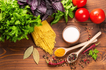 Raw pasta, vegetables, basil and spices on the wood table