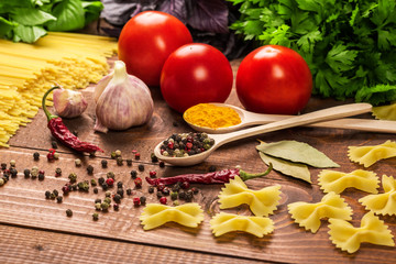 Raw pasta, vegetables, basil and spices on the wood table