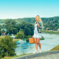 Hipster girl with vintage suitcase on the urban landscape. portrait of a beautiful blonde