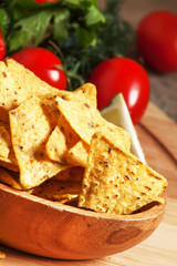 Nachos in wooden bowl with sauce, tomatoes and lime, selective f