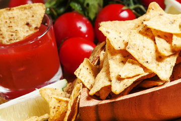 Nachos in wooden bowl with sauce, tomatoes and lime, selective f
