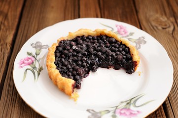 Juicy blueberry tart cut in white plate with pink carnation on w