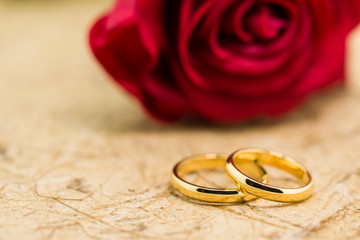 Wedding rings and artificial rose on brown background