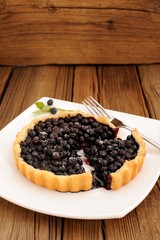 Homemade blueberry tart cut in square white plate with fork and