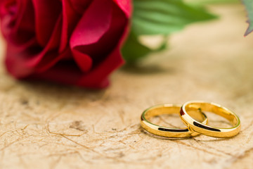Wedding rings and artificial rose on brown background